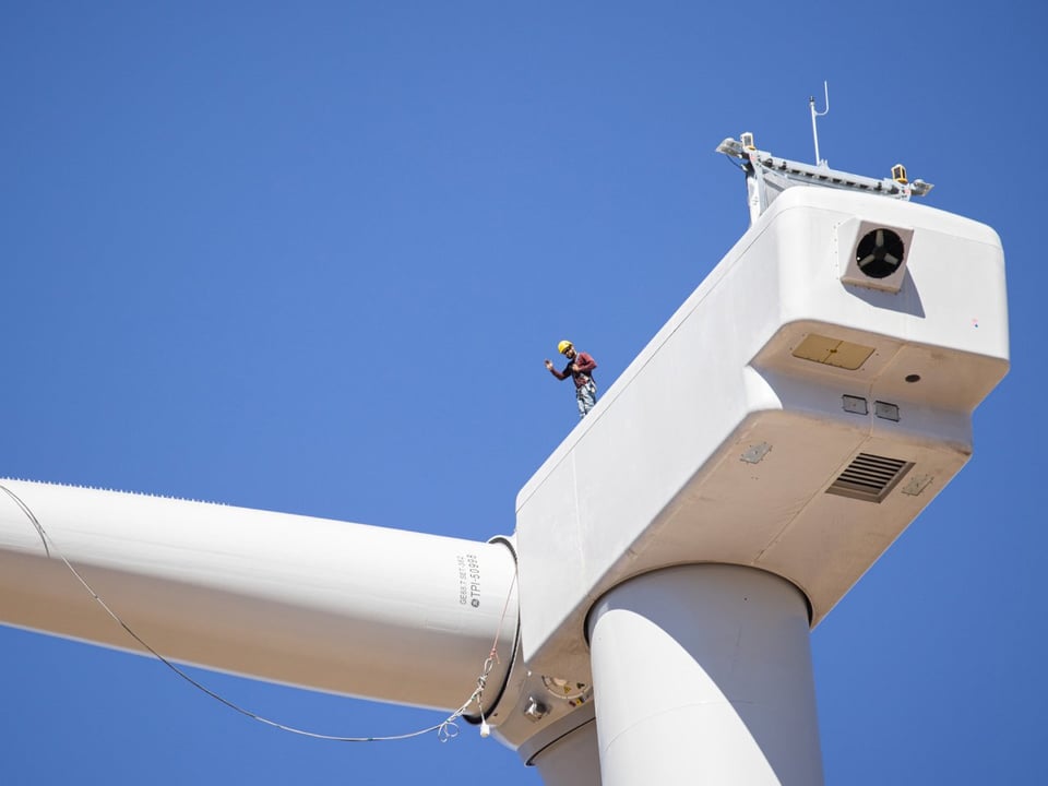 From a distance a worker stands atop wind turbine