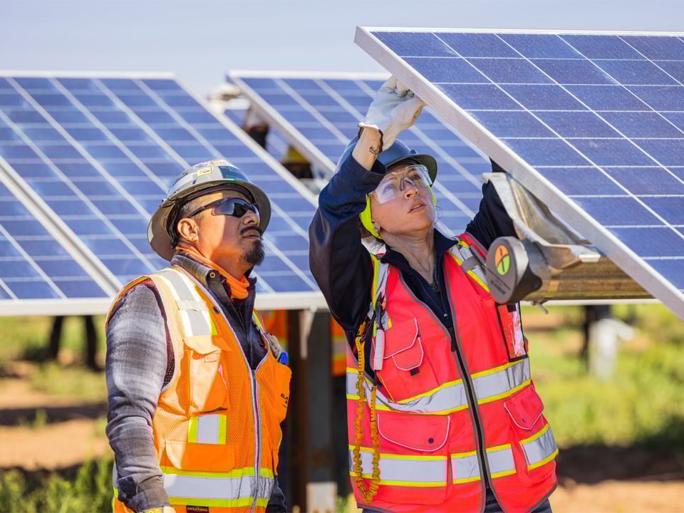One worker working on a solar panel while the other observes