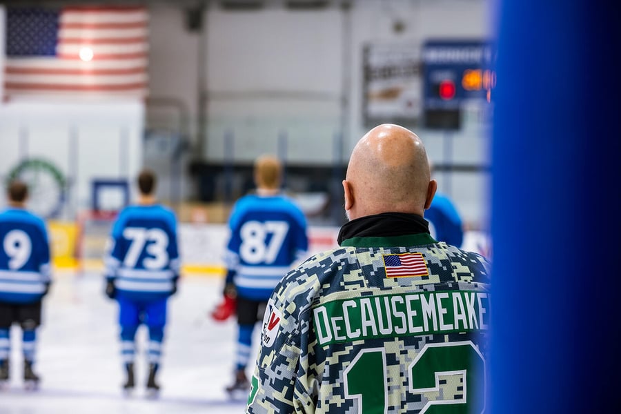 Hockey players standing on the ice towards the American flag while the national anthem is sung